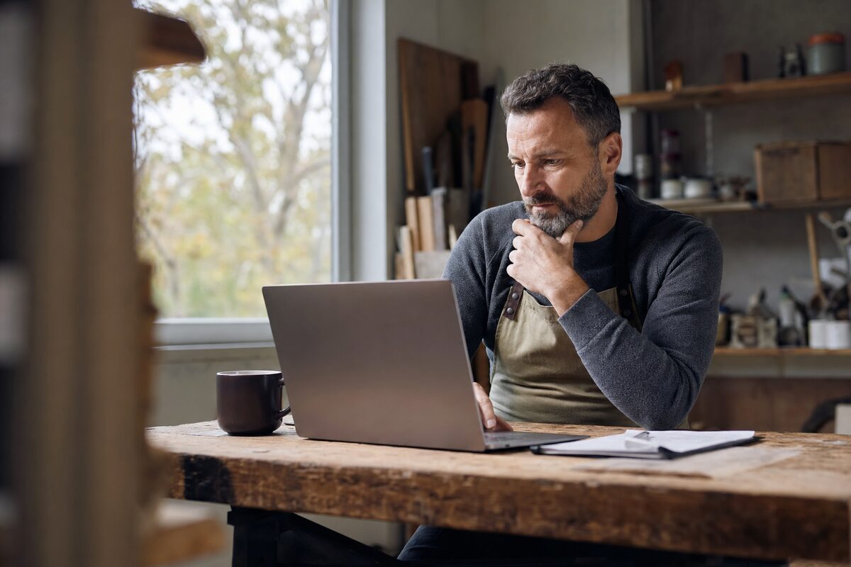 A small business owner reviewing their website on a laptop at a tidy wooden desk, warm natural light from a window